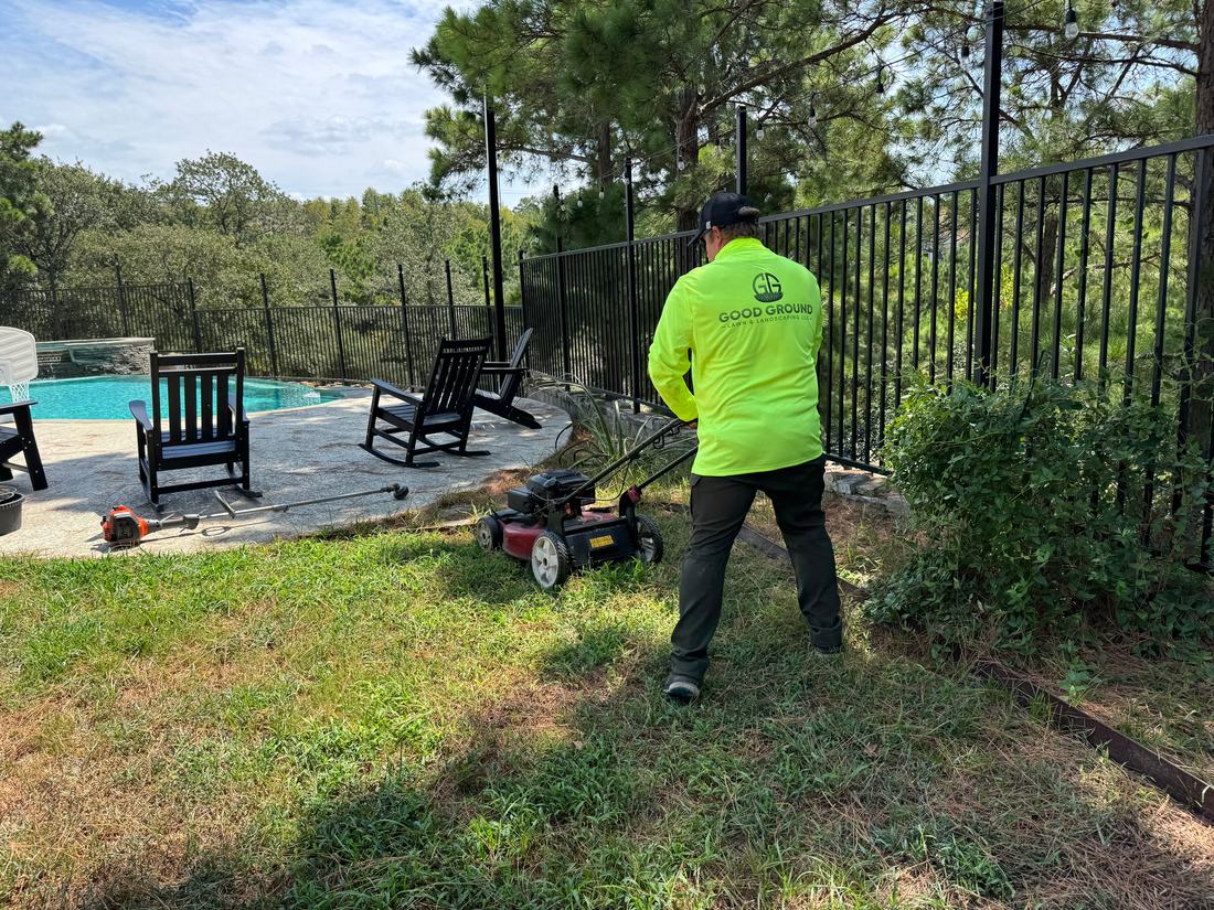 A Good Ground crew member in a Good Ground shirt mowing a back lawn beside a pool.